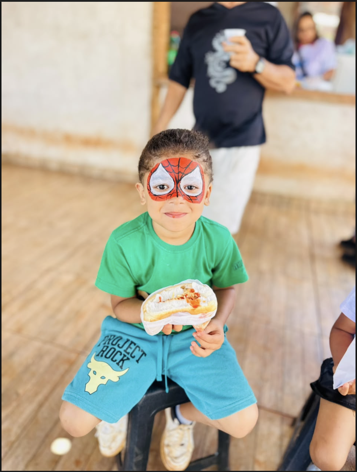 Criança com pintura facial segurando um lanche durante a festa.
