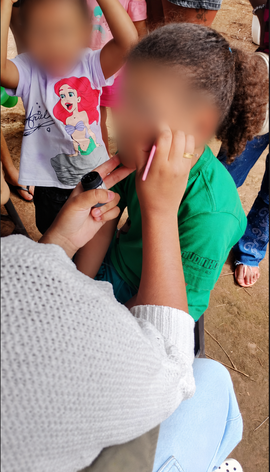 Cuidado e criatividade na pintura facial. Rostos desfocados para preservar a identidade das crianças.